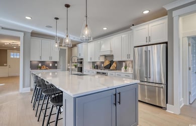 Kitchen featuring appliances with stainless steel finishes, white cabinets, a kitchen bar, a center island with sink, and decorative light fixtures