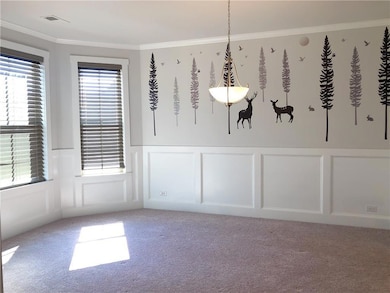 Unfurnished dining area with a decorative wall, ornamental molding, a wainscoted wall, and carpet floors
