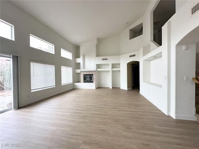 Unfurnished living room with a high ceiling, light wood finished floors, a glass covered fireplace, arched walkways, and built in features