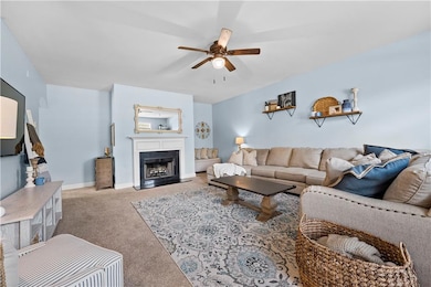 Living area with a ceiling fan, carpet, and a fireplace with flush hearth