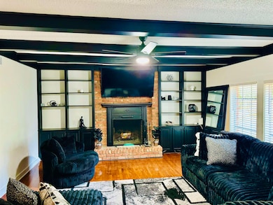 Living room featuring beam ceiling, wood finished floors, and a brick fireplace