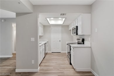 Kitchen with light countertops, white cabinetry, stainless steel appliances, and light wood-style floors