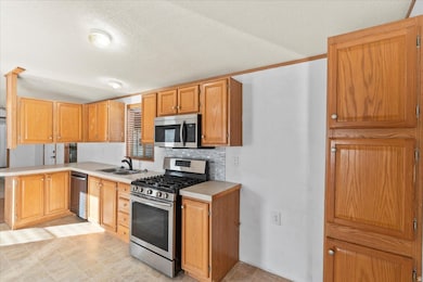 Kitchen featuring appliances with stainless steel finishes, light countertops, a peninsula, a textured ceiling, and tasteful backsplash
