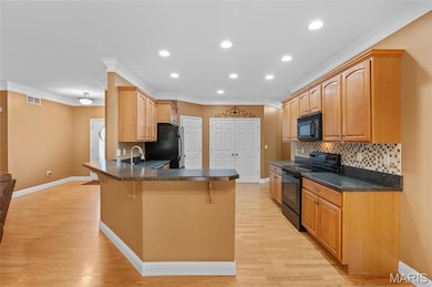 Kitchen featuring black appliances, a kitchen breakfast bar, dark countertops, ornamental molding, and recessed lighting