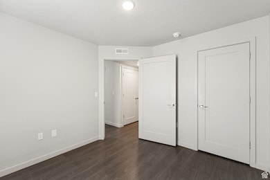 Unfurnished bedroom featuring dark wood-style flooring and baseboards