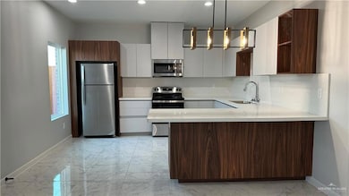 Kitchen with tasteful backsplash, white cabinetry, sink, decorative light fixtures, and appliances with stainless steel finishes
