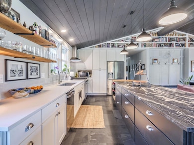 Kitchen featuring lofted ceiling, dark stone countertops, open shelves, stainless steel appliances, and wall chimney range hood