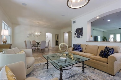 Living room with arched walkways, stone tile floors, ornamental molding, recessed lighting, and a chandelier