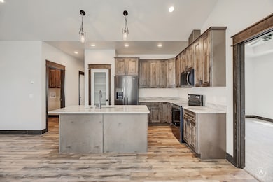 Kitchen with black range with electric cooktop, stainless steel refrigerator with ice dispenser, a kitchen island with sink, decorative light fixtures, and light stone countertops