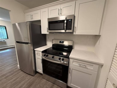 Kitchen featuring appliances with stainless steel finishes, dark wood-style flooring, decorative backsplash, white cabinetry, and a baseboard radiator