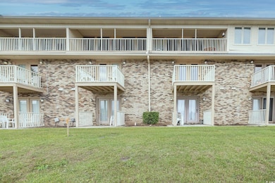 Rear view of property with a balcony, a lawn, and brick siding
