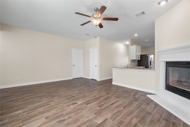Unfurnished living room featuring a glass covered fireplace, dark wood-style flooring, a ceiling fan, and recessed lighting