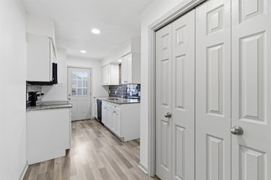 Kitchen featuring white cabinetry, dark stone counters, light wood finished floors, backsplash, and recessed lighting