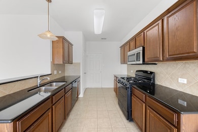 Kitchen with decorative backsplash, stainless steel appliances, hanging light fixtures, brown cabinetry, and dark stone countertops