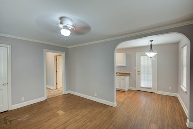 Unfurnished room with wood finished floors, crown molding, a ceiling fan, and arched walkways