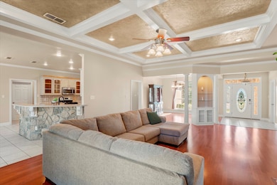 Living room with crown molding, ornate columns, a chandelier, beamed ceiling, and coffered ceiling