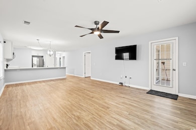 Unfurnished living room featuring ceiling fan, light wood-style flooring, and baseboards