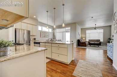 Kitchen featuring light stone counters, appliances with stainless steel finishes, an island with sink, and wood finished floors