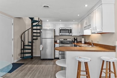 Kitchen with appliances with stainless steel finishes, wood finished floors, a textured ceiling, a peninsula, and white cabinetry
