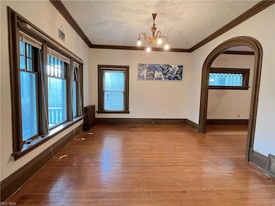 Wood floored spare room with a notable chandelier, radiator heating unit, and ornamental molding