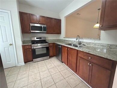 Kitchen with stainless steel appliances, light tile patterned floors, light stone countertops, and decorative light fixtures
