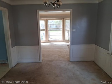 Unfurnished dining area with a decorative wall, wainscoting, light colored carpet, and a chandelier