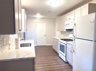 Kitchen with backsplash, white appliances, light stone countertops, dark wood-style floors, and white cabinets