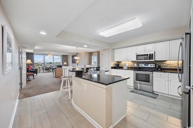 Kitchen featuring appliances with stainless steel finishes, white cabinets, an island with sink, backsplash, and a kitchen breakfast bar
