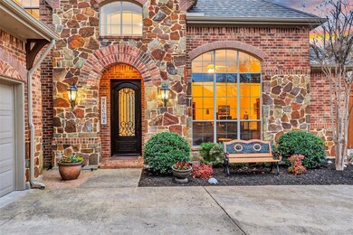 Courtyard view shows beautiful stonework, landscaped beds, brick paved porch and striking wood, wrought iron and glass front door.