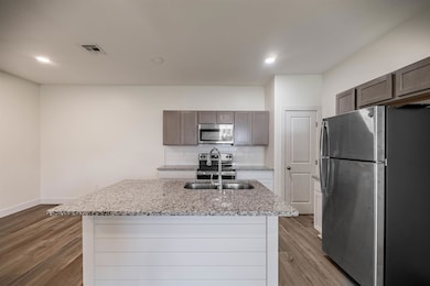 Kitchen featuring appliances with stainless steel finishes, light stone counters, decorative backsplash, light wood-type flooring, and a center island with sink