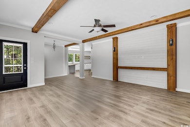 Unfurnished living room featuring beamed ceiling, light wood finished floors, and ceiling fan
