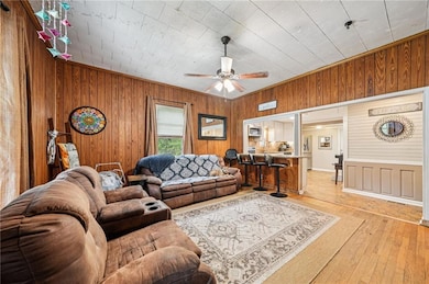 Living room featuring light wood finished floors, wooden walls, and ceiling fan