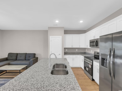 Kitchen with stainless steel appliances, light wood-style flooring, light stone counters, white cabinets, and recessed lighting
