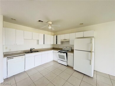 Kitchen featuring white appliances, white cabinets, light tile patterned floors, a ceiling fan, and under cabinet range hood