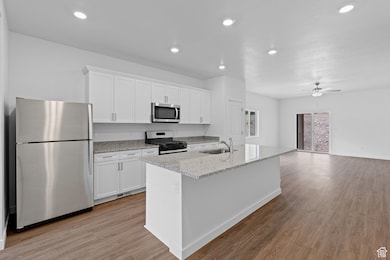 Kitchen featuring appliances with stainless steel finishes, light stone countertops, white cabinets, light wood-type flooring, and recessed lighting