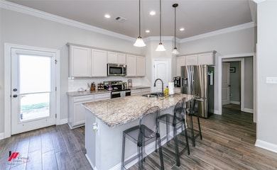 Kitchen featuring appliances with stainless steel finishes, backsplash, crown molding, white cabinets, and a kitchen island with sink
