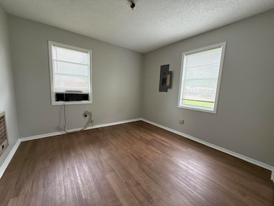 Empty room with a textured ceiling, dark wood-style flooring, electric panel, and baseboards