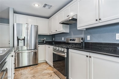 Kitchen with stainless steel appliances, white cabinets, under cabinet range hood, and dark stone countertops
