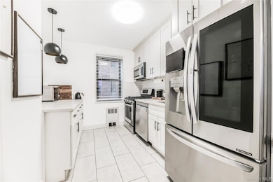 Kitchen with stainless steel appliances, white cabinetry, decorative backsplash, light tile patterned floors, and hanging light fixtures