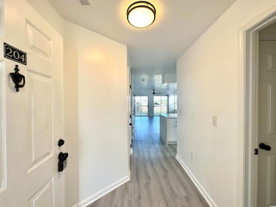 Hallway with light wood-type flooring, visible vents, and baseboards