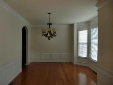 Unfurnished dining area with a decorative wall, wainscoting, arched walkways, dark wood-style flooring, and a chandelier