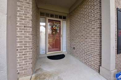 Covered front porch with brick exterior, storm door, and side-light windows creating a welcoming entrance.