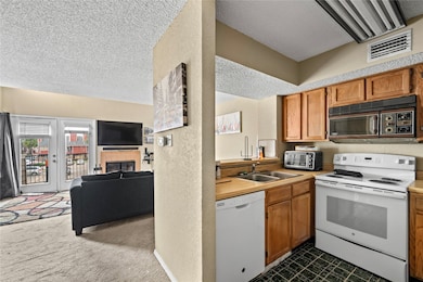 Kitchen featuring a textured ceiling, white appliances, open floor plan, light countertops, and a fireplace
