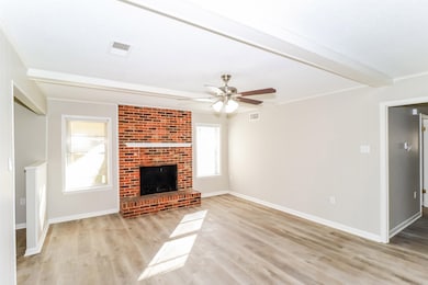 Unfurnished living room featuring light wood-style flooring, a ceiling fan, a fireplace, and beamed ceiling