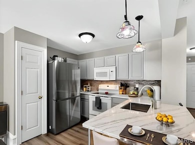 Kitchen with white appliances, decorative backsplash, decorative light fixtures, dark wood-type flooring, and light stone countertops