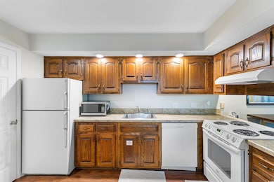 Kitchen with white appliances, a sink, under cabinet range hood, and light countertops