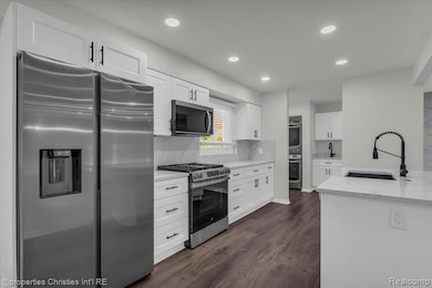 Kitchen featuring appliances with stainless steel finishes, white cabinets, recessed lighting, light stone counters, and dark wood-style flooring