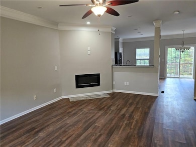 Unfurnished living room with ornamental molding, ceiling fan, dark wood finished floors, baseboards, and a chandelier