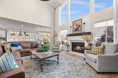 Living area with wood finished floors, a towering ceiling, a glass covered fireplace, crown molding, and a chandelier