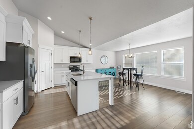 Kitchen with decorative light fixtures, a center island with sink, vaulted ceiling, white cabinets, and appliances with stainless steel finishes